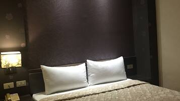 A hotel room with a bed, two white pillows, a nightstand with a phone, and a wall-mounted lamp.