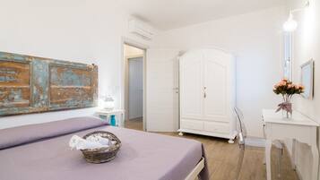 A bedroom with a bed, a wardrobe, a vanity with a mirror, and a wall-mounted air conditioner.