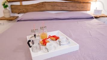 A neatly arranged breakfast tray on a bed with a wooden headboard, a white pillow, and a bedside table with a small plant and a clock.