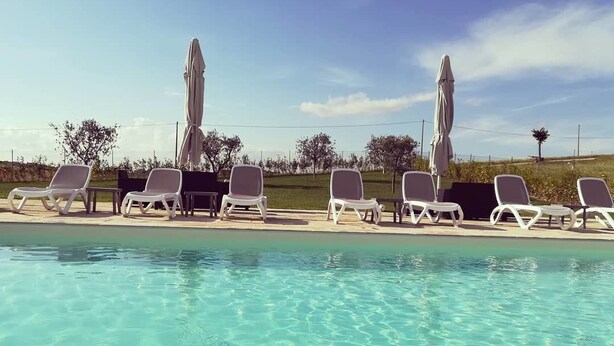Una piscina con agua cristalina, rodeada de sillas de descanso blancas y sombrillas.