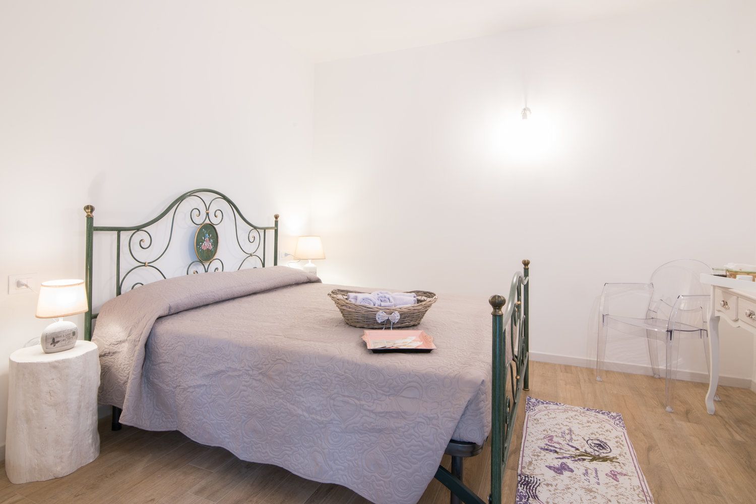 Um quarto bem arrumado com uma cama, luminárias de cabeceira, mesa de cabeceira, uma cadeira e um tapete pequeno.