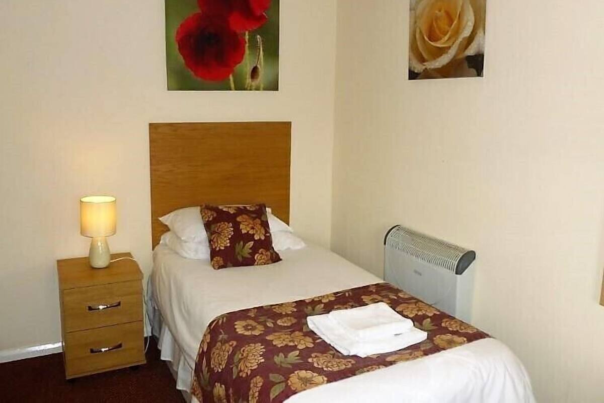 A hotel room with a bed, a nightstand with a lamp, and two wall-mounted pictures of flowers.