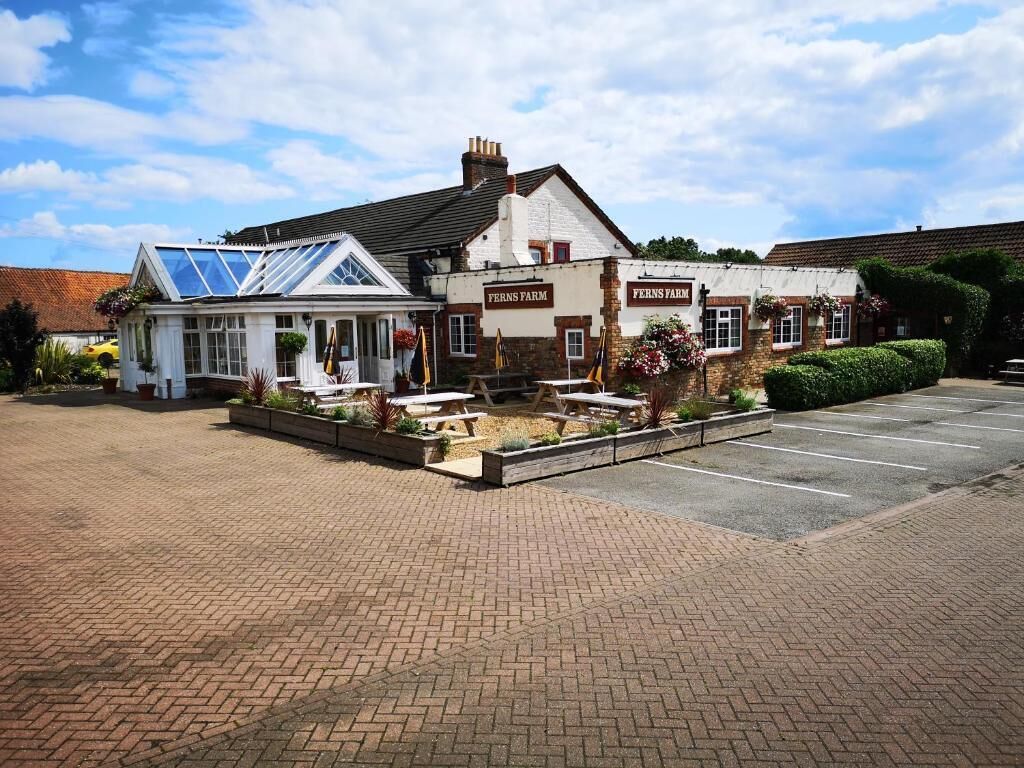 A building with 'Ferns Farm' signage, a covered outdoor seating area, and a parking lot.