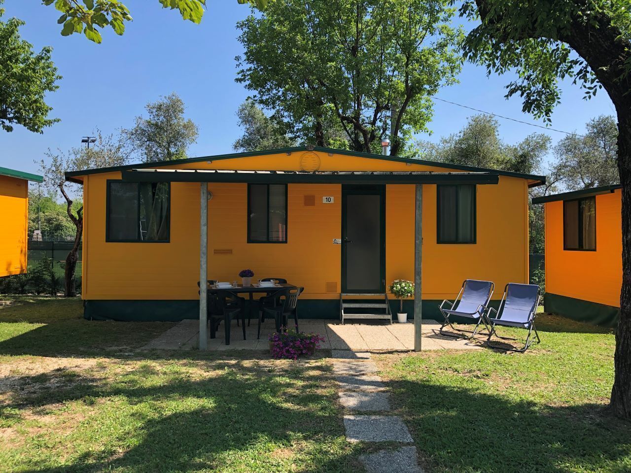 A yellow building with a door, windows, a table with chairs, and two lounge chairs.