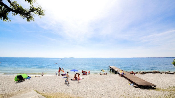 Ein Strand mit einem Holzsteg, entspannte Menschen und einem grünen Zelt.