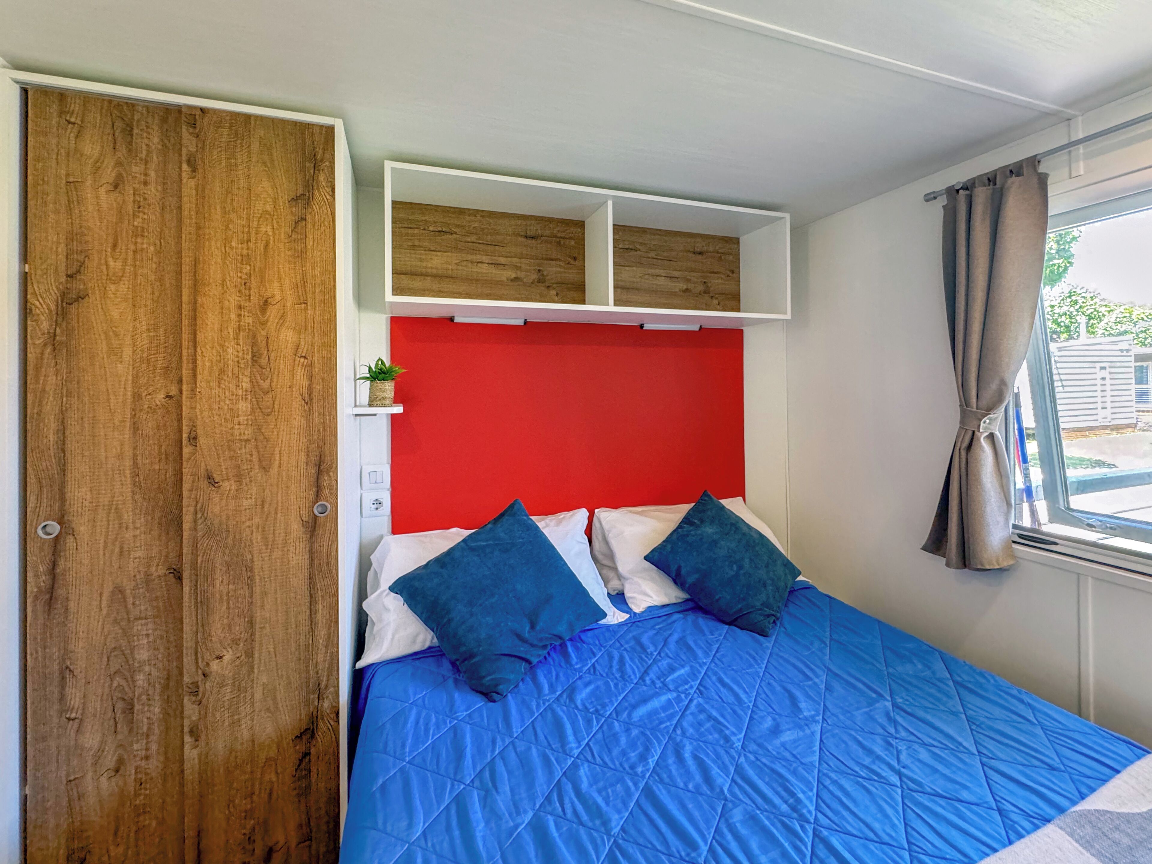 A bedroom with a blue bedspread, a red headboard, and a wooden wardrobe.