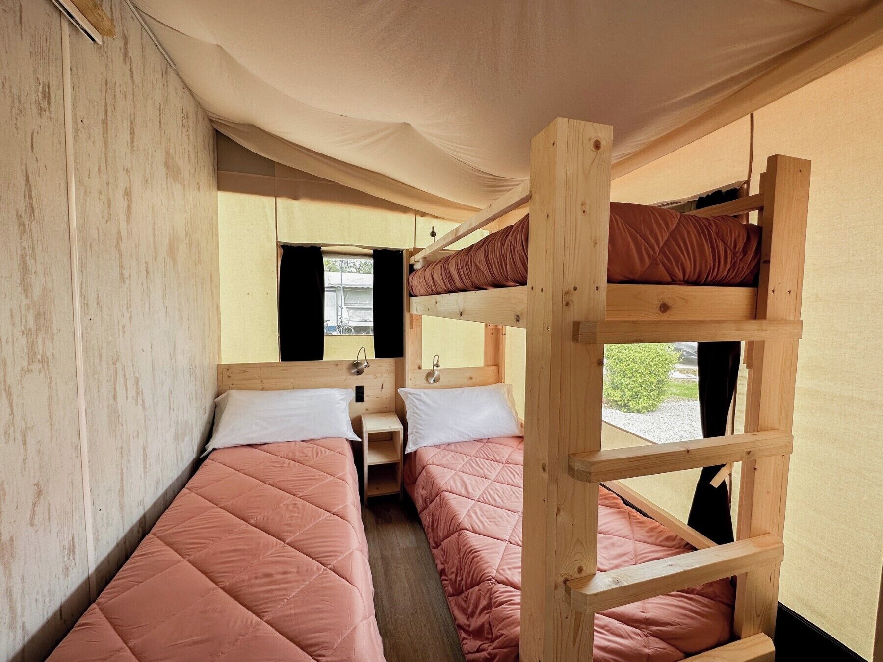 A bunk bed room with a window, wooden walls, and a curtain.