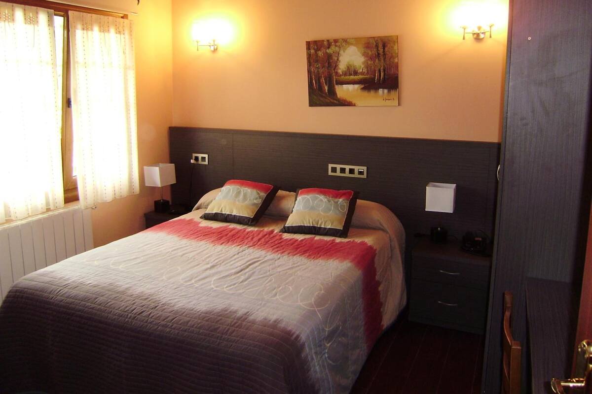 A hotel room with a large bed, two bedside lamps, a painting on the wall, and a window with curtains.
