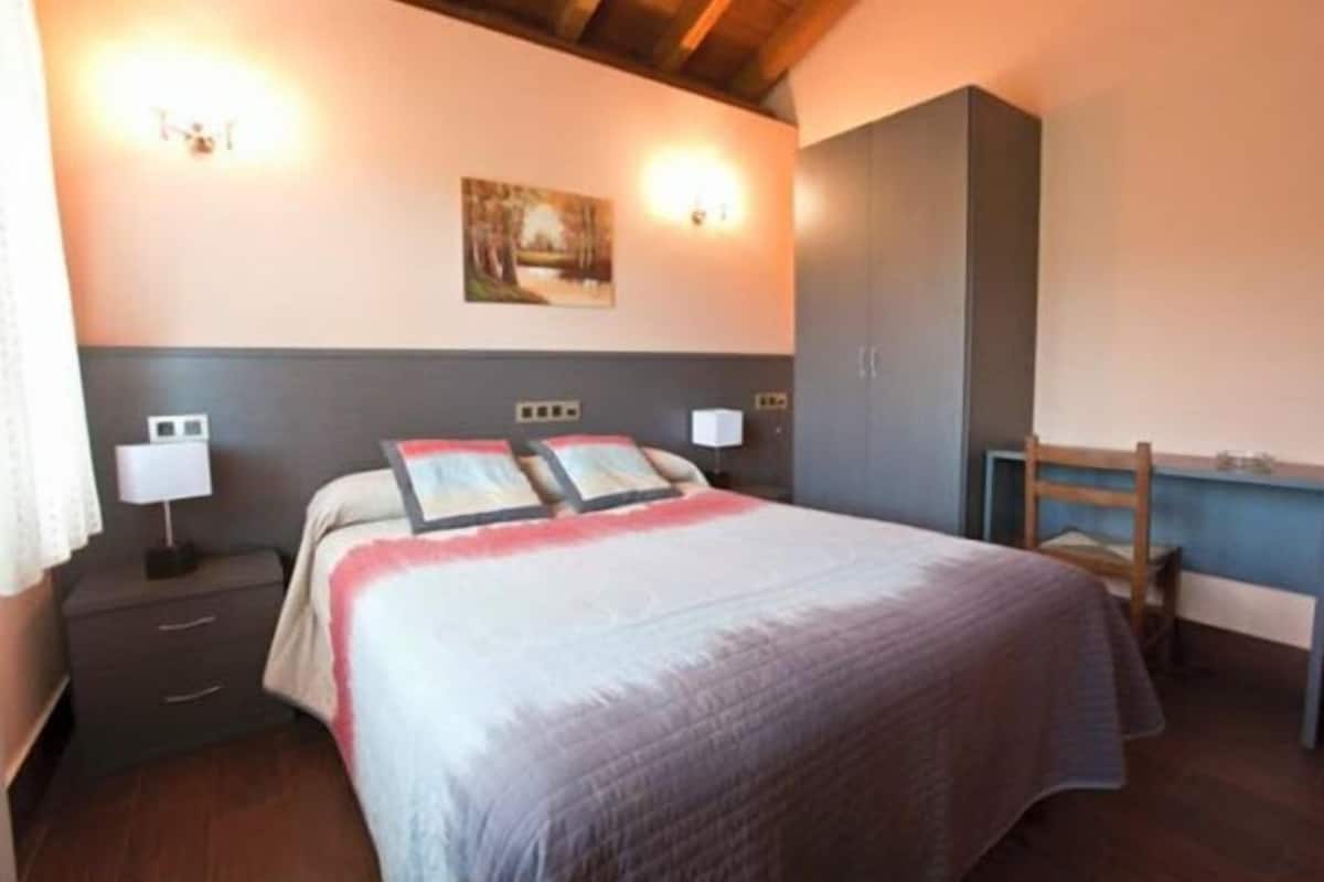 A bedroom with a bed, bedside tables, a desk, and a chair.