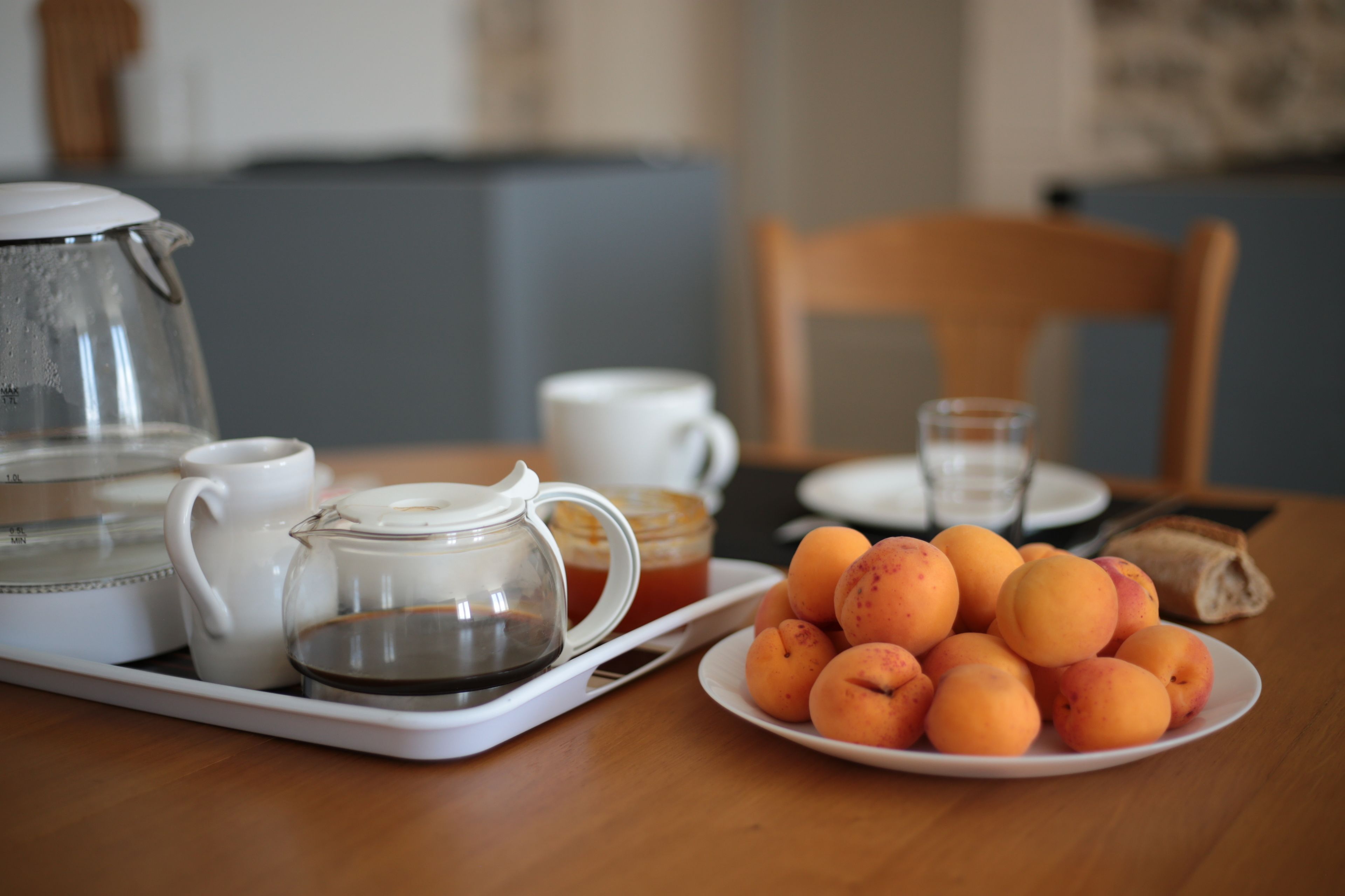 A breakfast setting with a tray containing a teapot, a cup, a glass, and a plate of peaches.