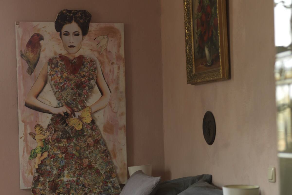 Une chambre à coucher avec un lit, des oreillers, une lampe, un tableau et une photo encadrée accrochée au mur.