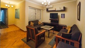 Un salon comprenant un canapé, des fauteuils, une table basse, un téléviseur et un élément décoratif mural.