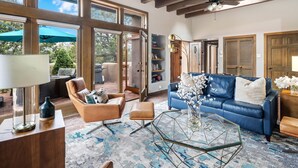 Un salon spacieux avec un canapé en cuir bleu, un fauteuil en cuir marron et une table basse en verre. De grandes fenêtres offrent une vue sur l’extérieur.