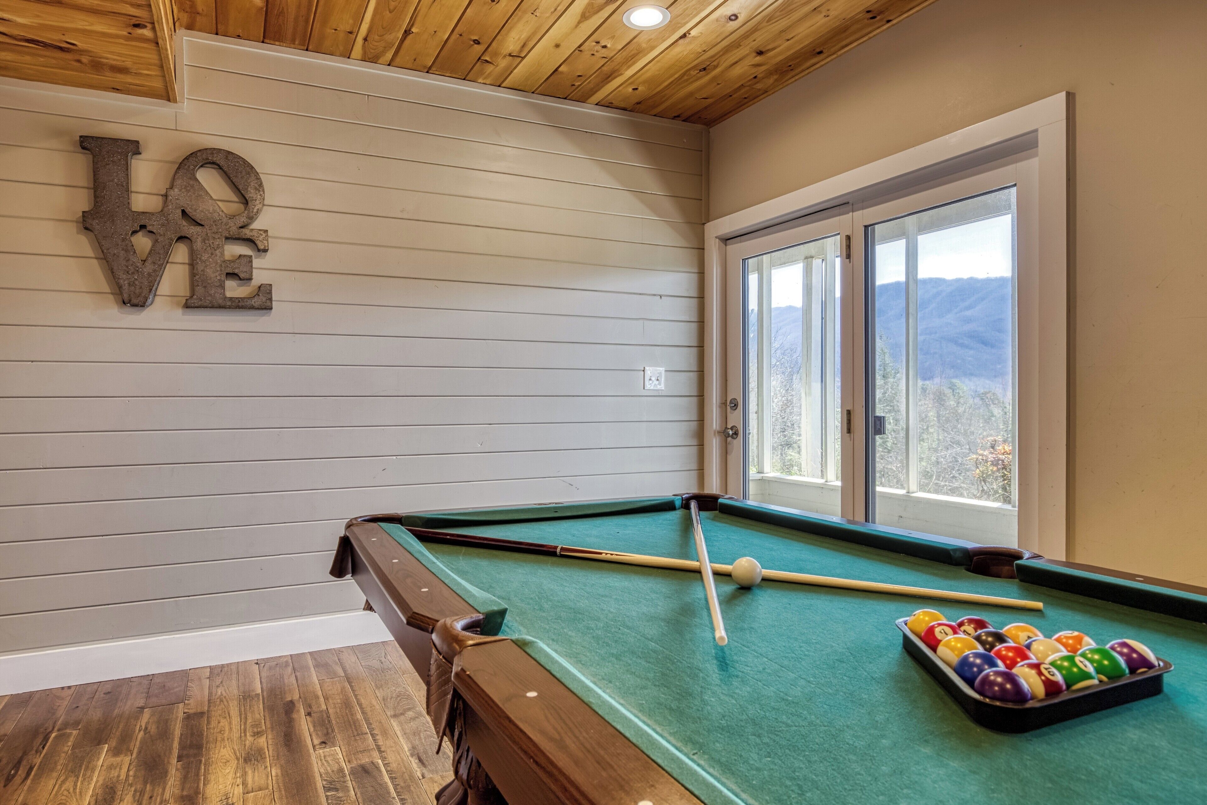 Une table de billard avec des billes, une queue et un panneau mural sur lequel est écrit le mot « AMOUR ».