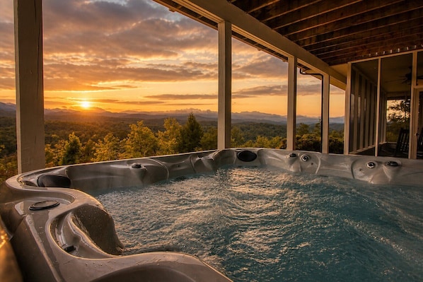 A hot tub with a panoramic view of mountains and sunset.