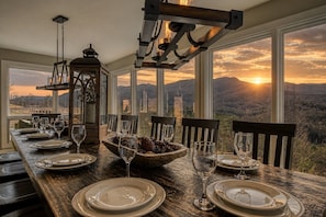 A dining table set with plates, glasses, and a centerpiece of pinecones and a lantern, overlooking a mountainous landscape.