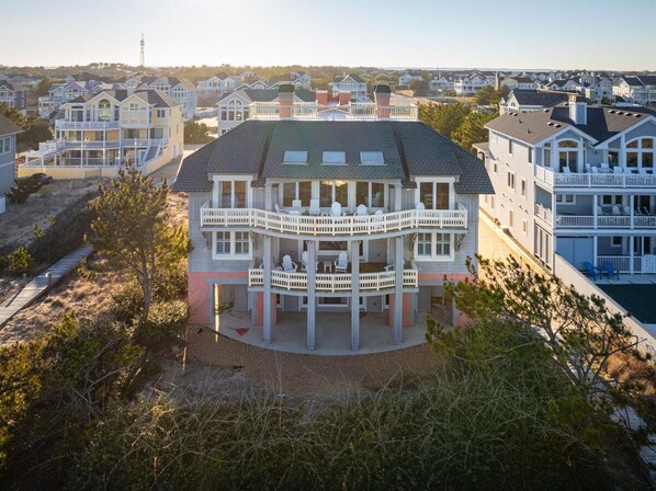 A multi-story house with a circular balcony, surrounded by other houses, and a clear sky.