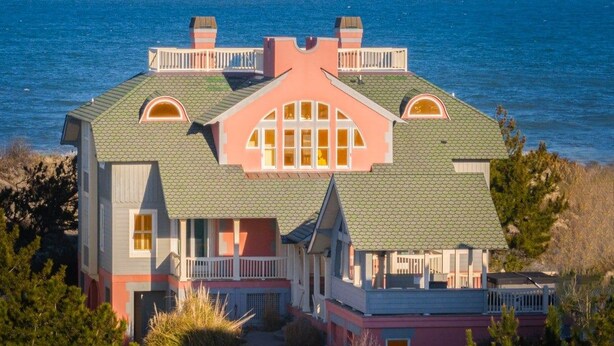 A large, multi-story house with a prominent gabled roof, multiple balconies, and a view of the ocean. - Ocean Front, Elevator, Pool, Hot Tub, Gated community and amazing views! BI-38 (Corolla)