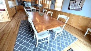 A dining area with a wooden table and chairs, a patterned rug, and a view of the kitchen in the background. - Ocean Front, Elevator, Pool, Hot Tub, Gated community and amazing views! BI-38 (Corolla)