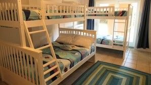 A room with bunk beds, a window with curtains, and a patterned rug. - Ocean Front, Elevator, Pool, Hot Tub, Gated community and amazing views! BI-38 (Corolla)