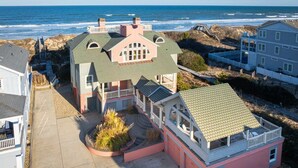 A beachfront property with a large house featuring a wrap-around porch, a separate garage, and a view of the ocean. - Ocean Front, Elevator, Pool, Hot Tub, Gated community and amazing views! BI-38 (Corolla)