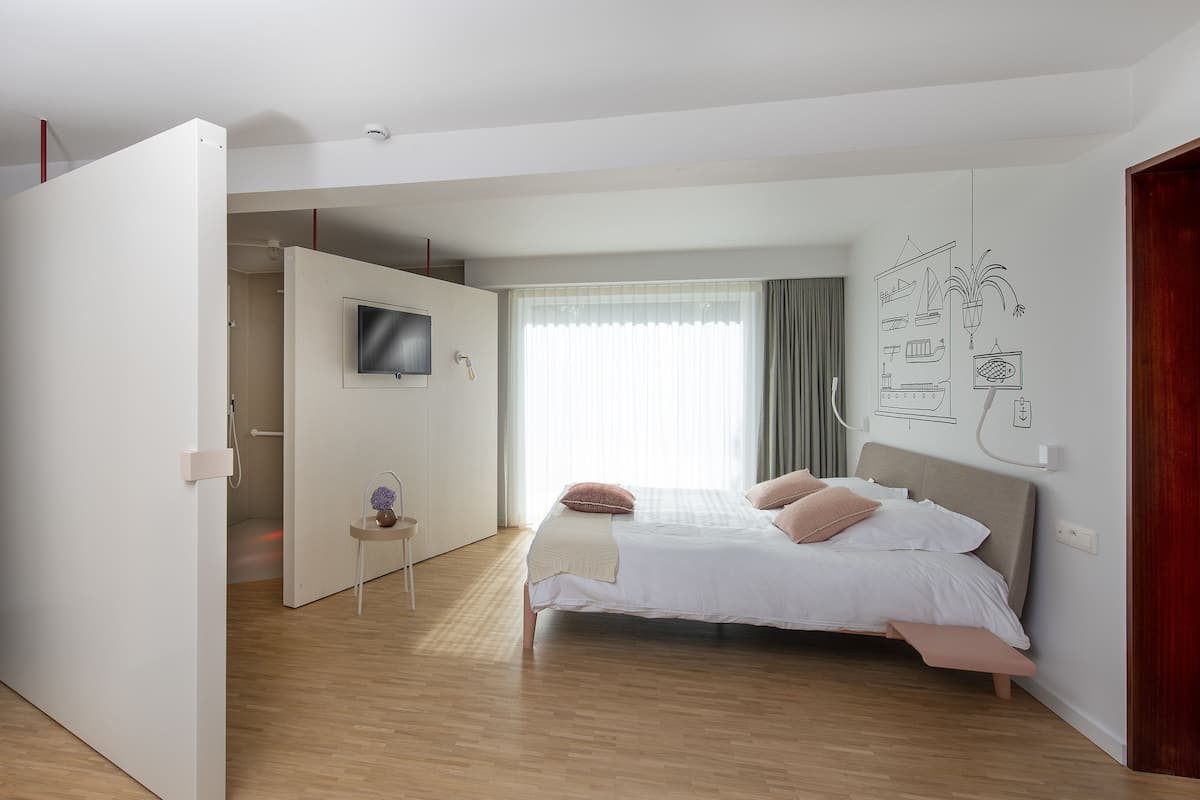 A modern bedroom with a bed, a TV, a small table with a vase, and a wall with nautical illustrations.