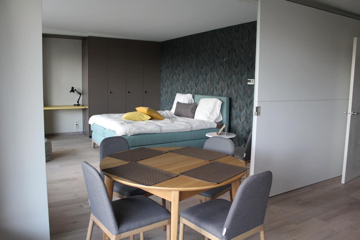 A modern bedroom with a bed, bedside table, and a desk with chairs.