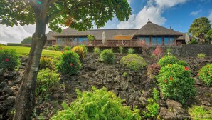 A building with a thatched roof, a balcony with a railing, and a garden with various plants and flowers. - Bubble Lodge Ile aux Cerfs (Trou d'Eau Douce)