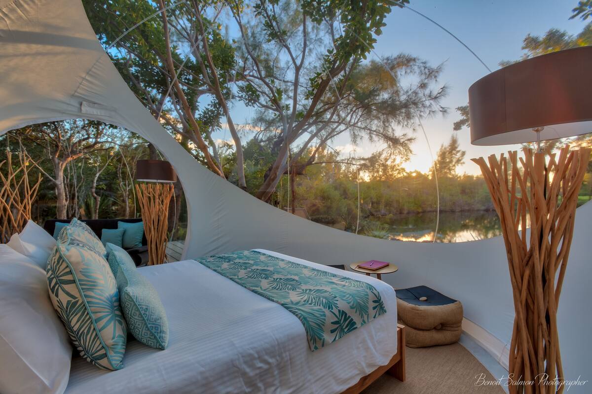 A tent-style bedroom with a bed, pillows, a bedside table, and a lamp.