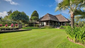 A thatched-roof building with a covered outdoor seating area, surrounded by well-maintained gardens and palm trees. - Bubble Lodge Ile aux Cerfs (Trou d'Eau Douce)