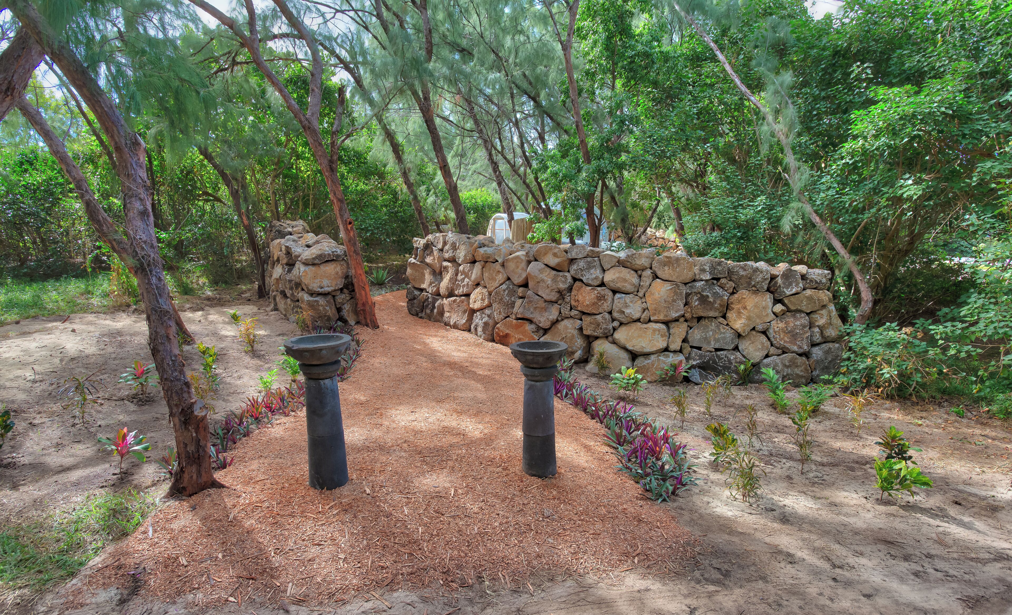 A stone wall with a pathway leading through a forested area.