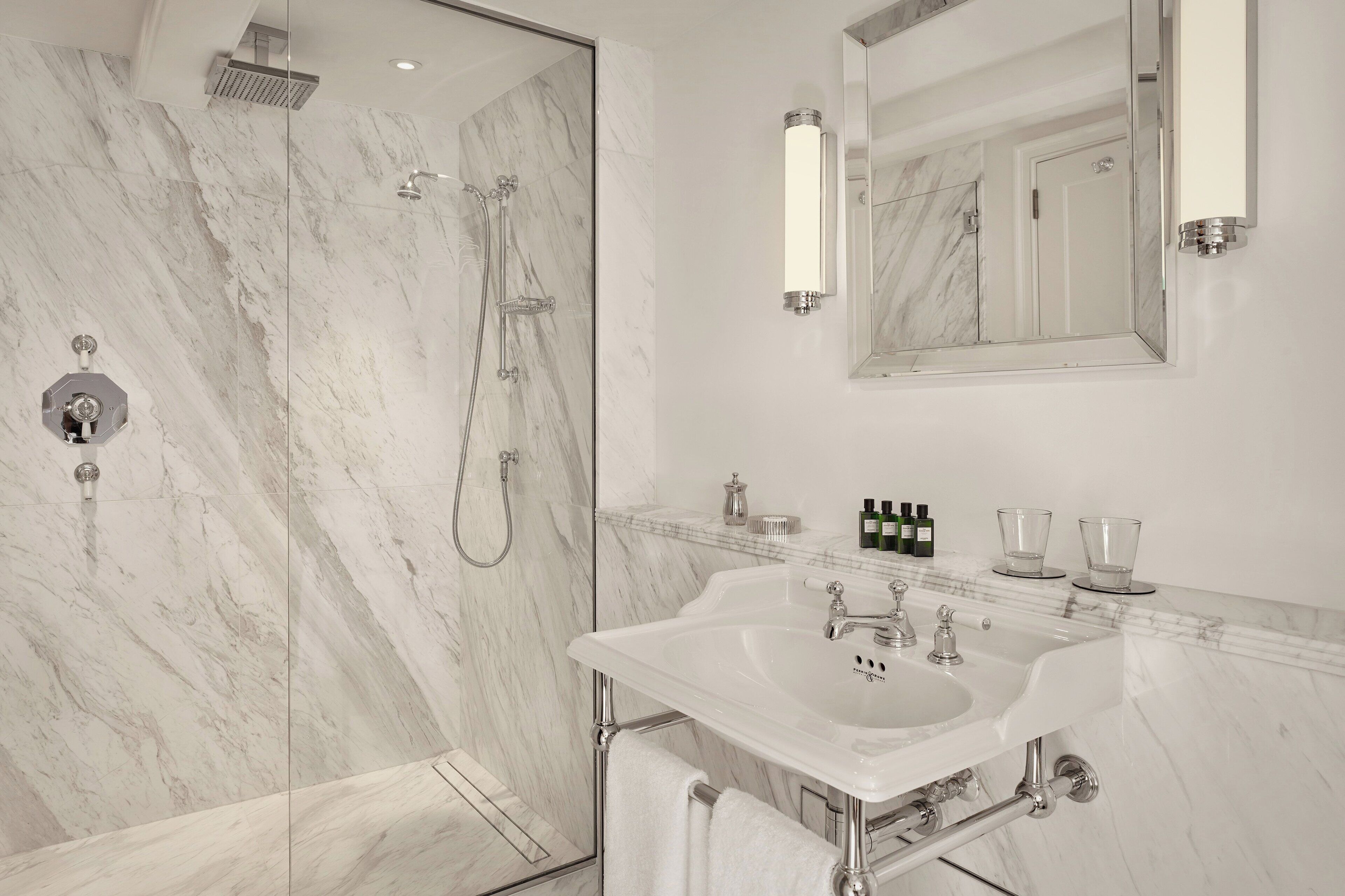 A modern bathroom with a marble shower, a large mirror, and a sink with two faucets.
