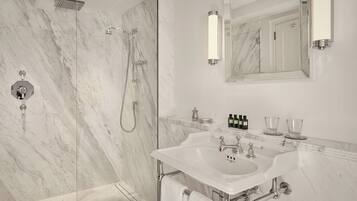 A modern bathroom with a marble shower, a large mirror, and a sink with two faucets.