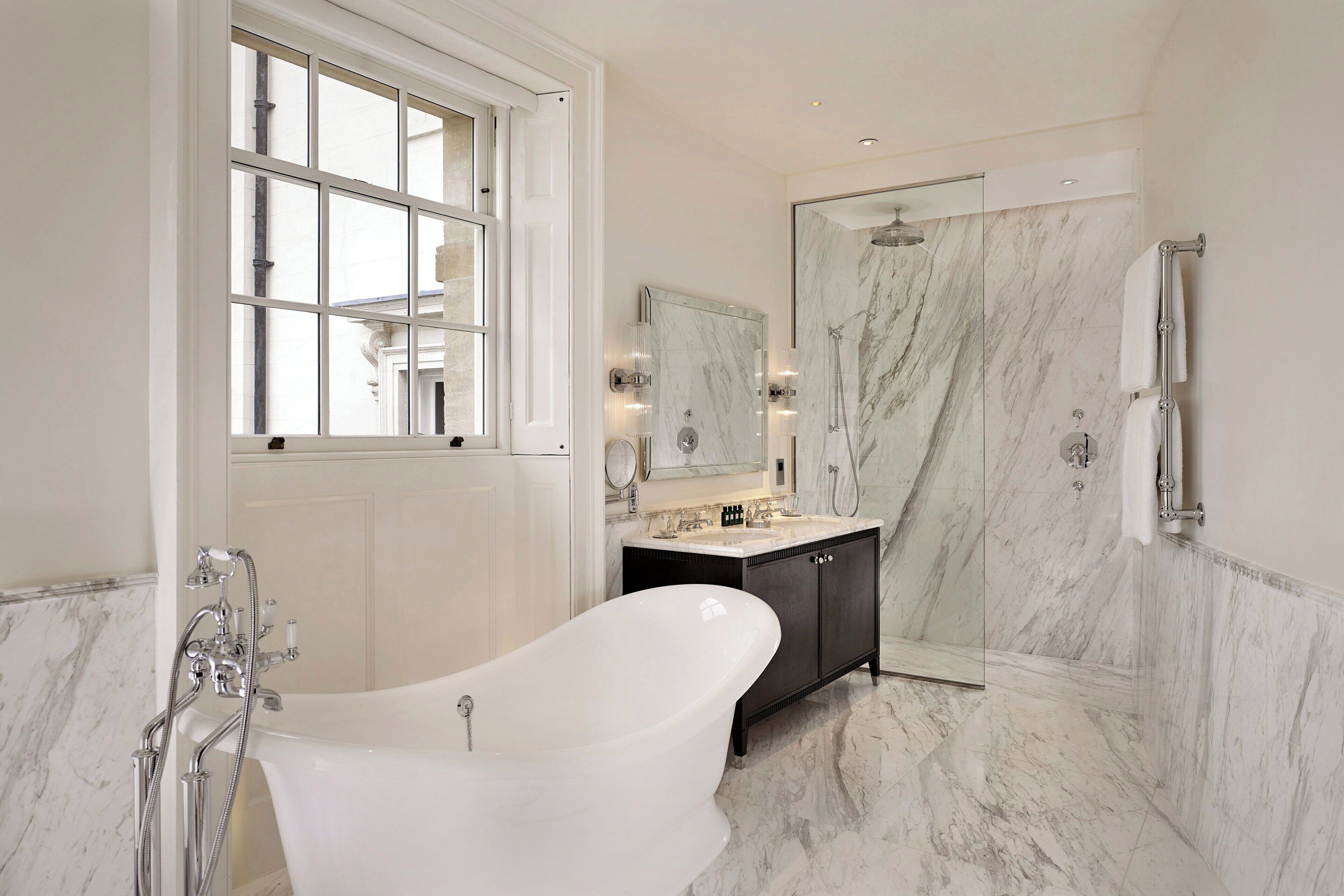A bathroom with a freestanding bathtub, a glass-enclosed shower, and a marble-tiled floor.