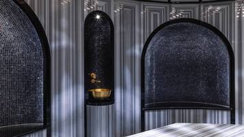 Un baño moderno con un espejo grande, un lavamanos dorado y una pared con azulejos.