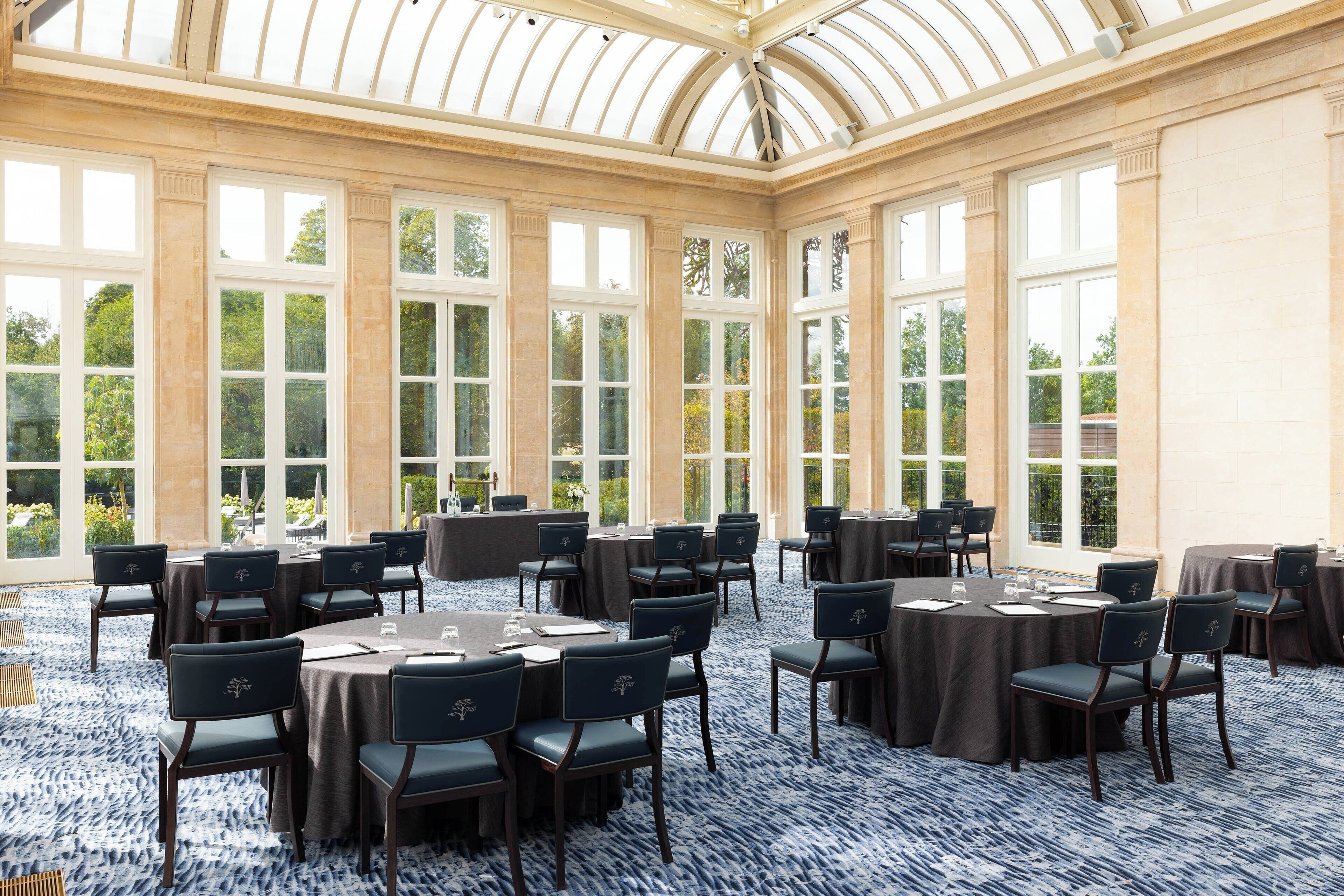 Une salle de conférence dotée de tables et de chaises rondes, de grandes fenêtres et d’un plafond haut.