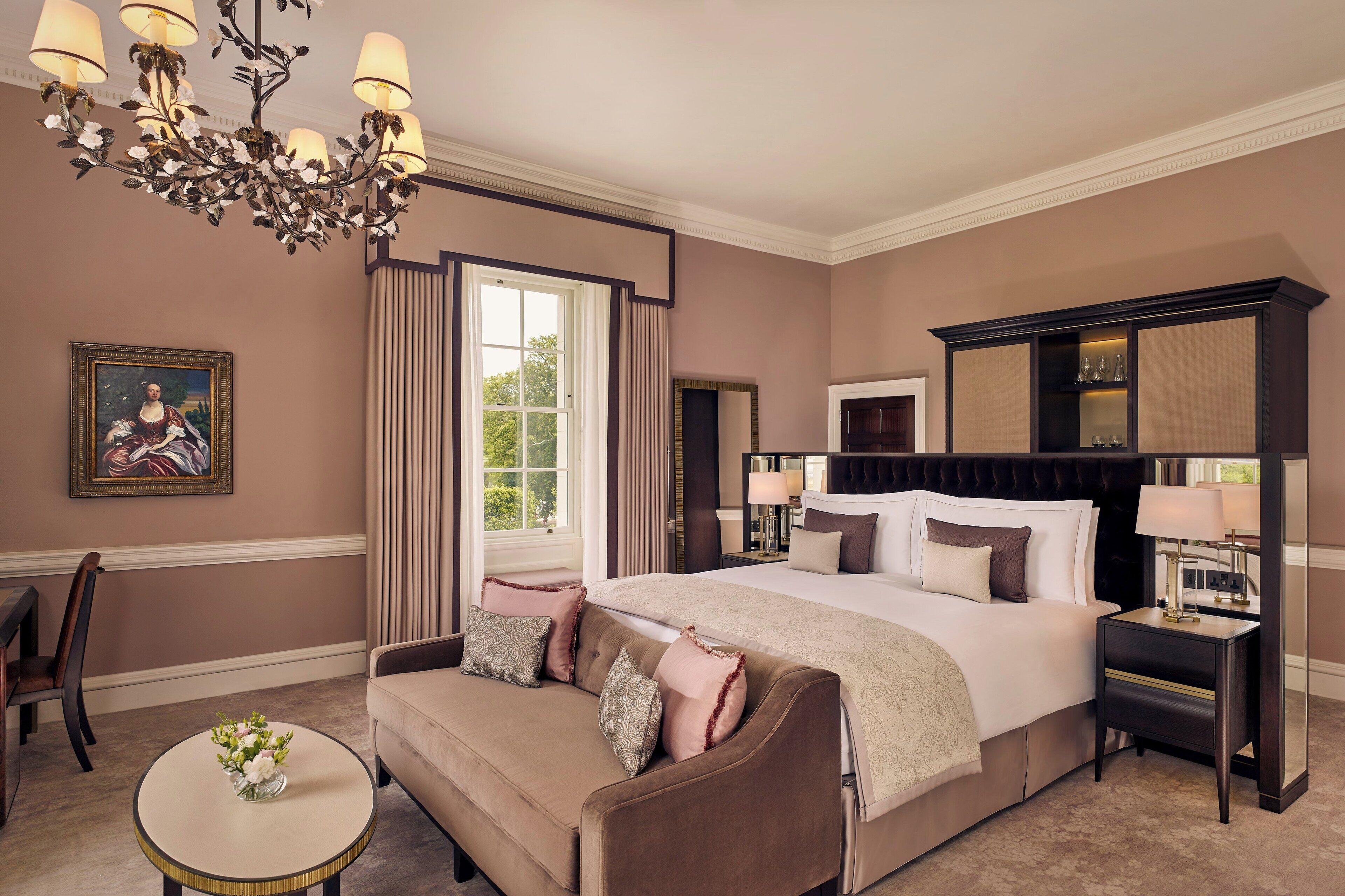 A spacious bedroom with a large bed, a sitting area with a sofa, a round coffee table, and a chandelier.