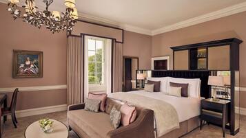 A spacious bedroom with a large bed, a sitting area with a sofa, a round coffee table, and a chandelier.
