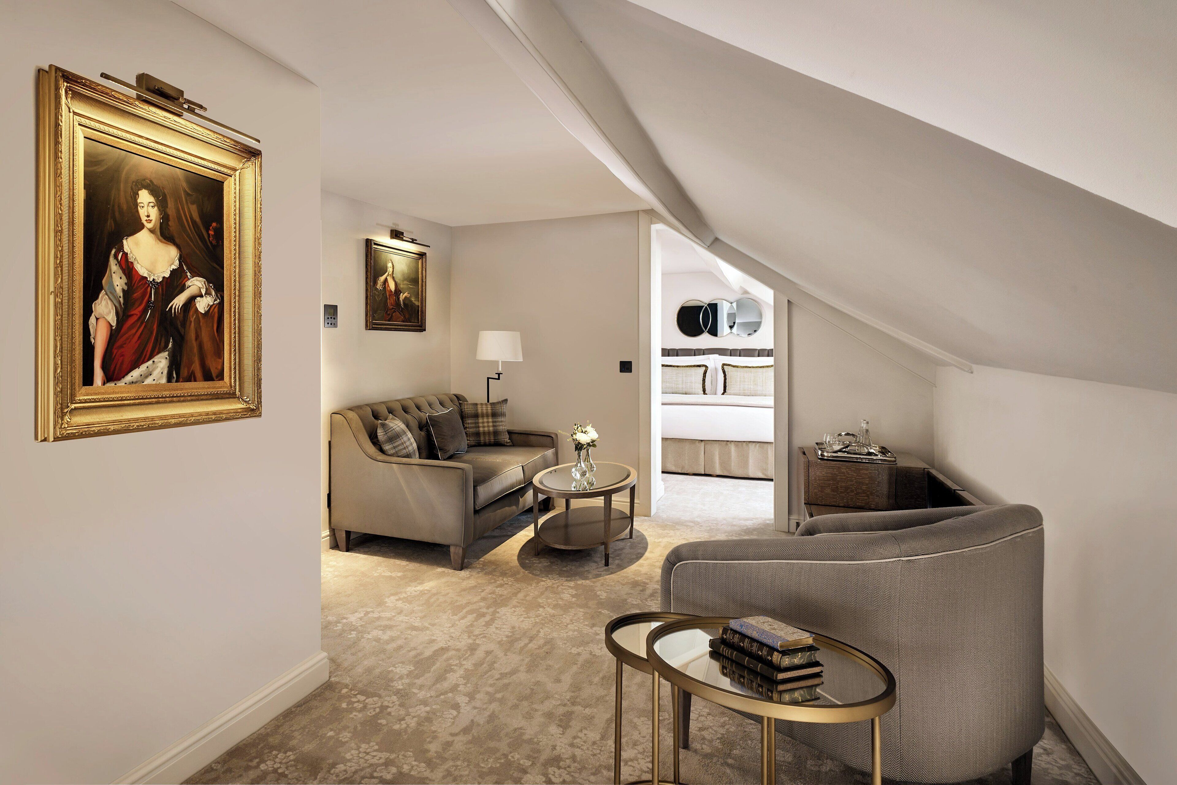 Una sala de estar moderna con sofá, sillón y mesa de centro, un cuadro en la pared y una escalera que conduce a un nivel superior.
