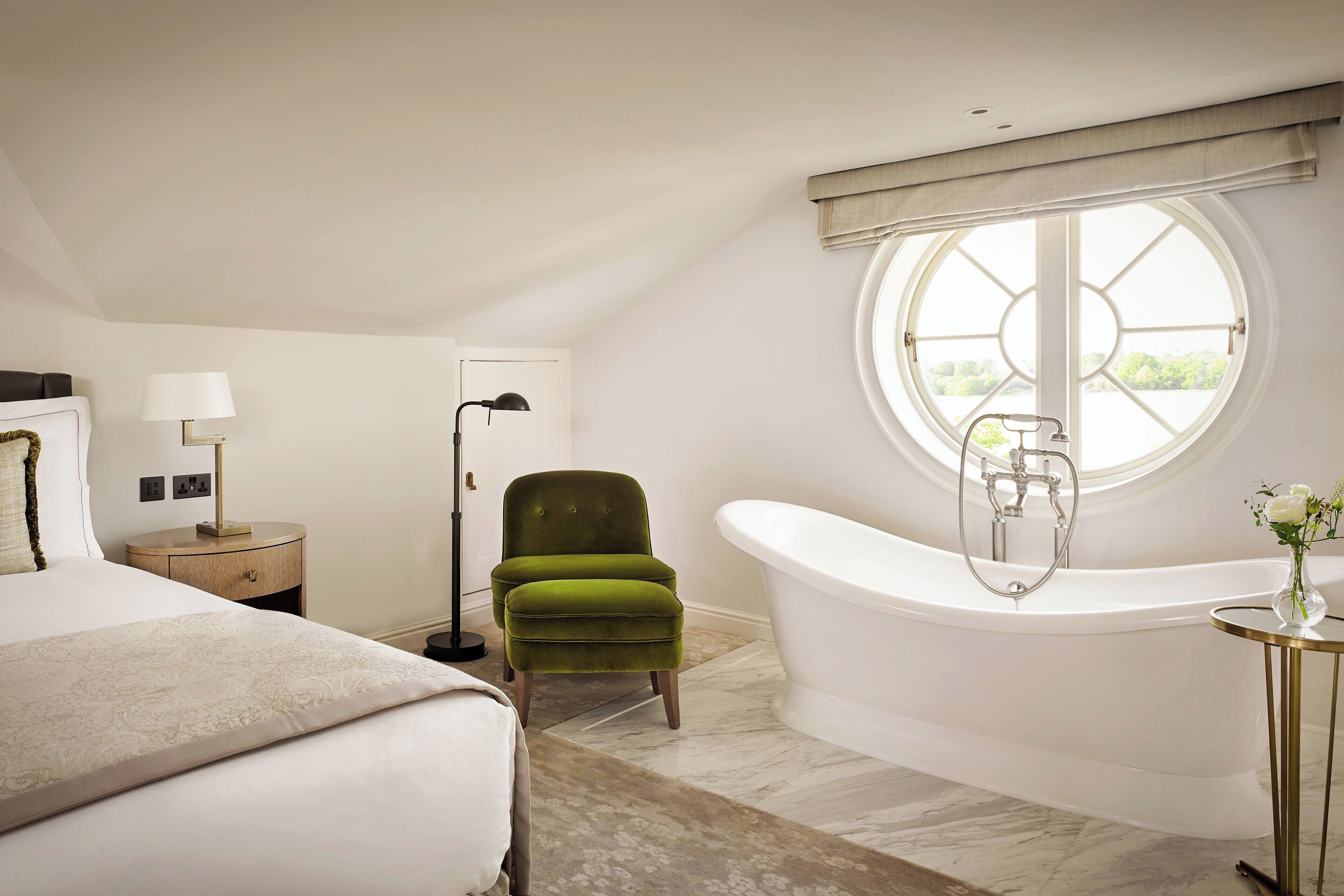 Une chambre à coucher avec un grand lit, un fauteuil vert, une baignoire blanche et une fenêtre donnant sur un beau paysage.