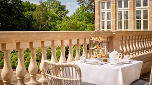 An outdoor dining area with a table set for tea service, surrounded by a balustrade and lush greenery. - The Langley, a Luxury Collection Hotel, Buckinghamshire (Slough)