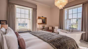 A spacious bedroom with a large bed, a bathtub, and a view of the outdoors through large windows.