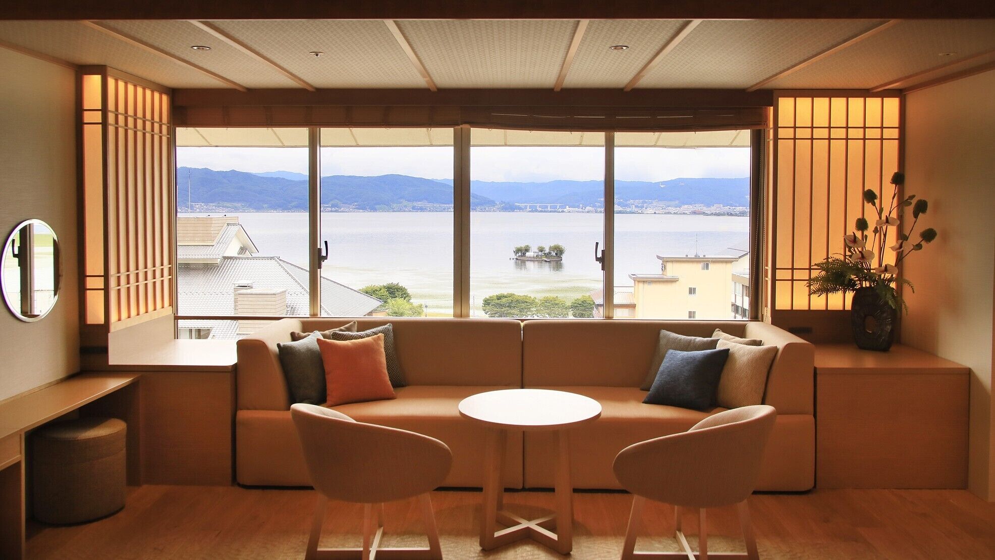 Una habitación con un sofá, dos sillones, una mesita y vistas a una masa de agua y edificios a lo lejos.