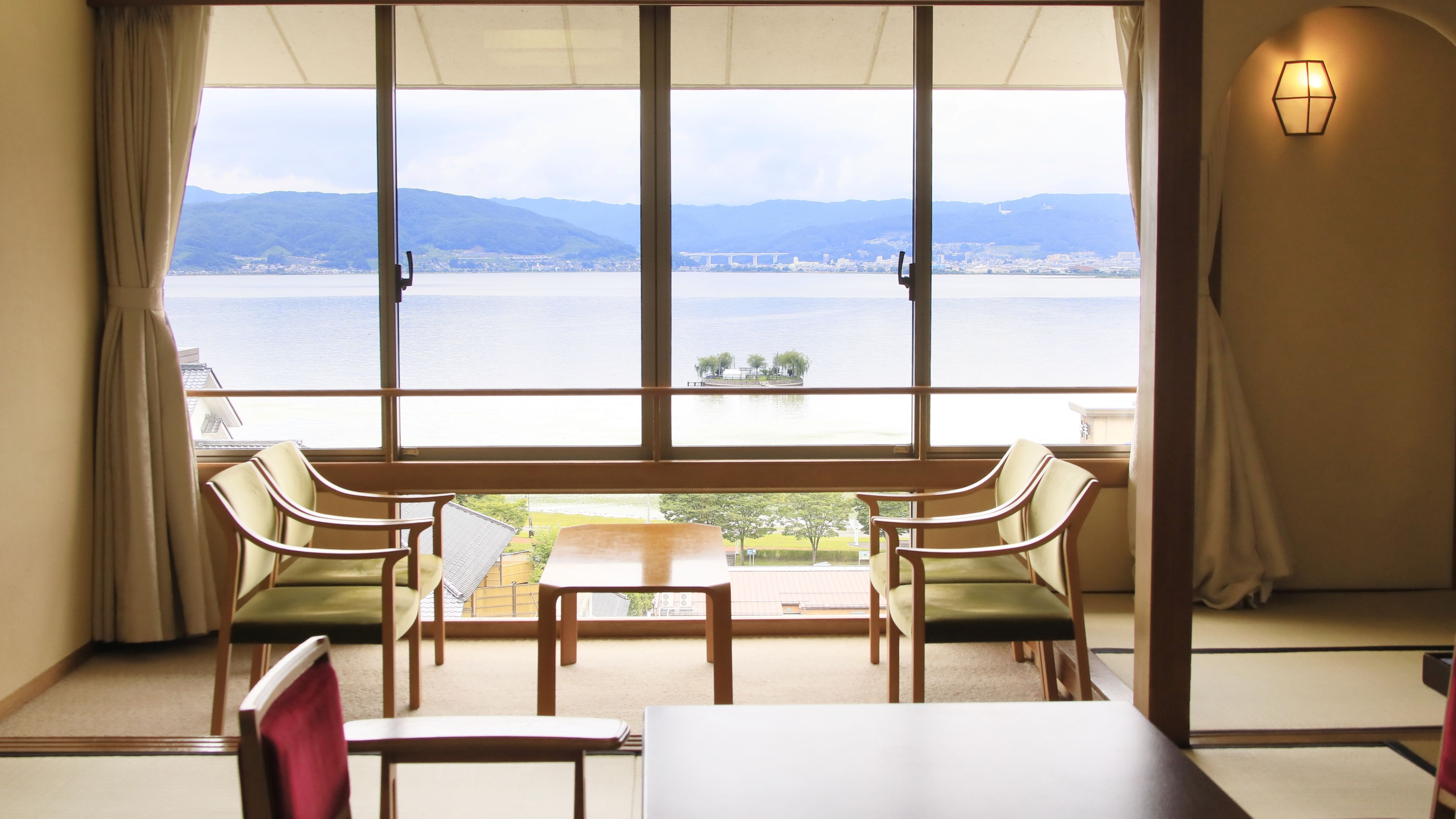 Une pièce dotée d’une grande fenêtre donnant sur un plan d’eau et sur des montagnes lointaines, et comprenant une table et quatre chaises.
