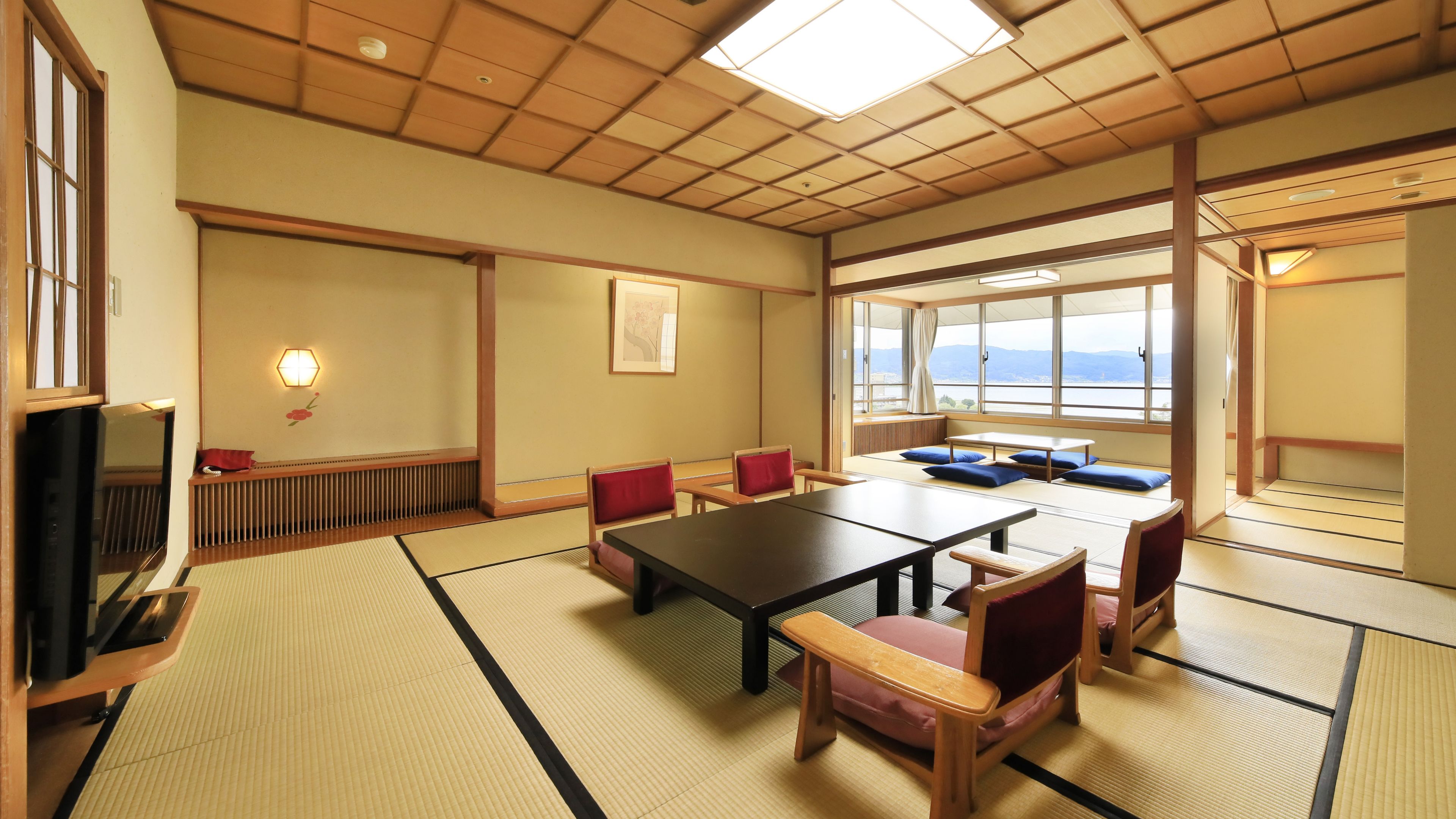 Una stanza tradizionale giapponese con pavimento in tatami, un tavolino e cuscini rossi.