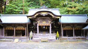 A traditional Japanese building with a central entrance, two small trees, and a stone-paved ground. - Hamanoyu (Suwa)