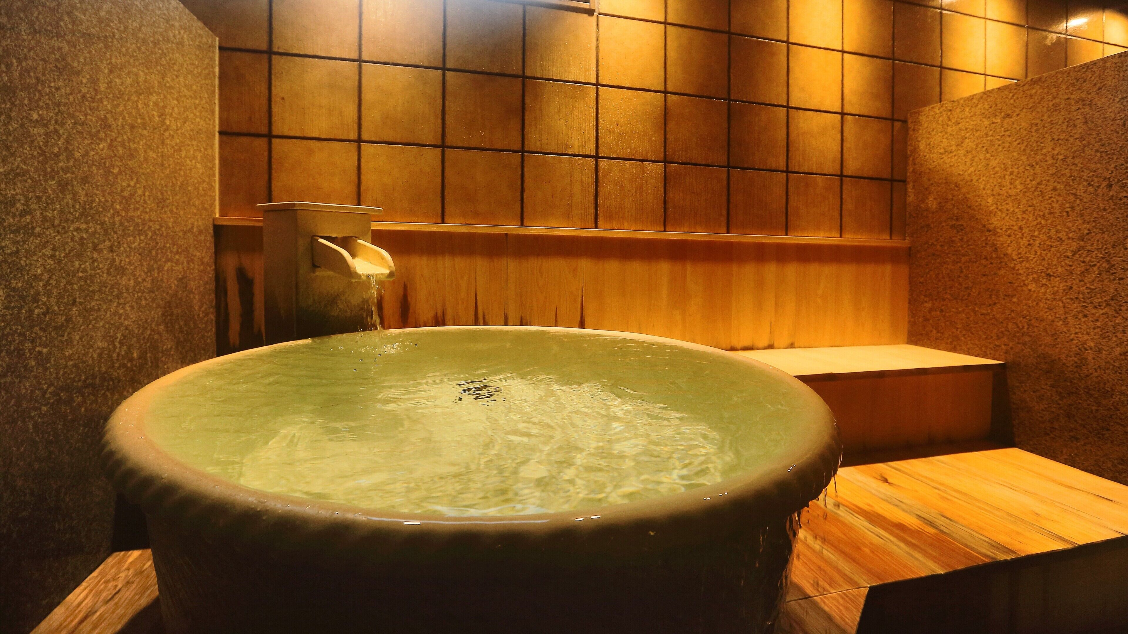 Een hottub in een houten badruimte met een betegelde muur en een houten bank.