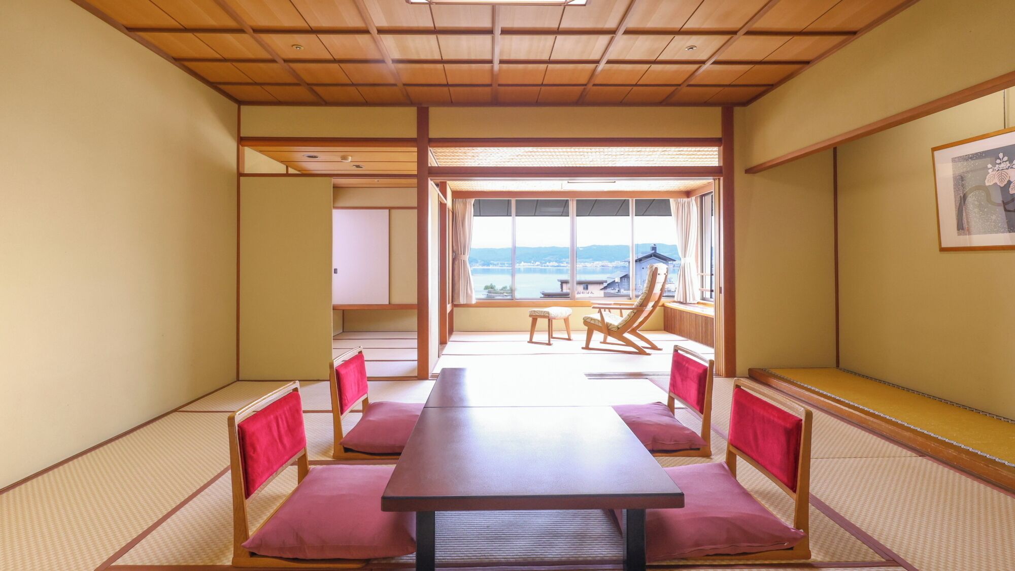 Una habitación japonesa tradicional con suelo de tatami, una mesa de madera baja y cojines rojos.
