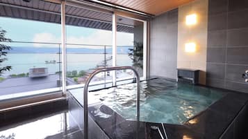 A modern indoor swimming pool with a glass barrier, a view of a body of water, and a wooden ceiling.