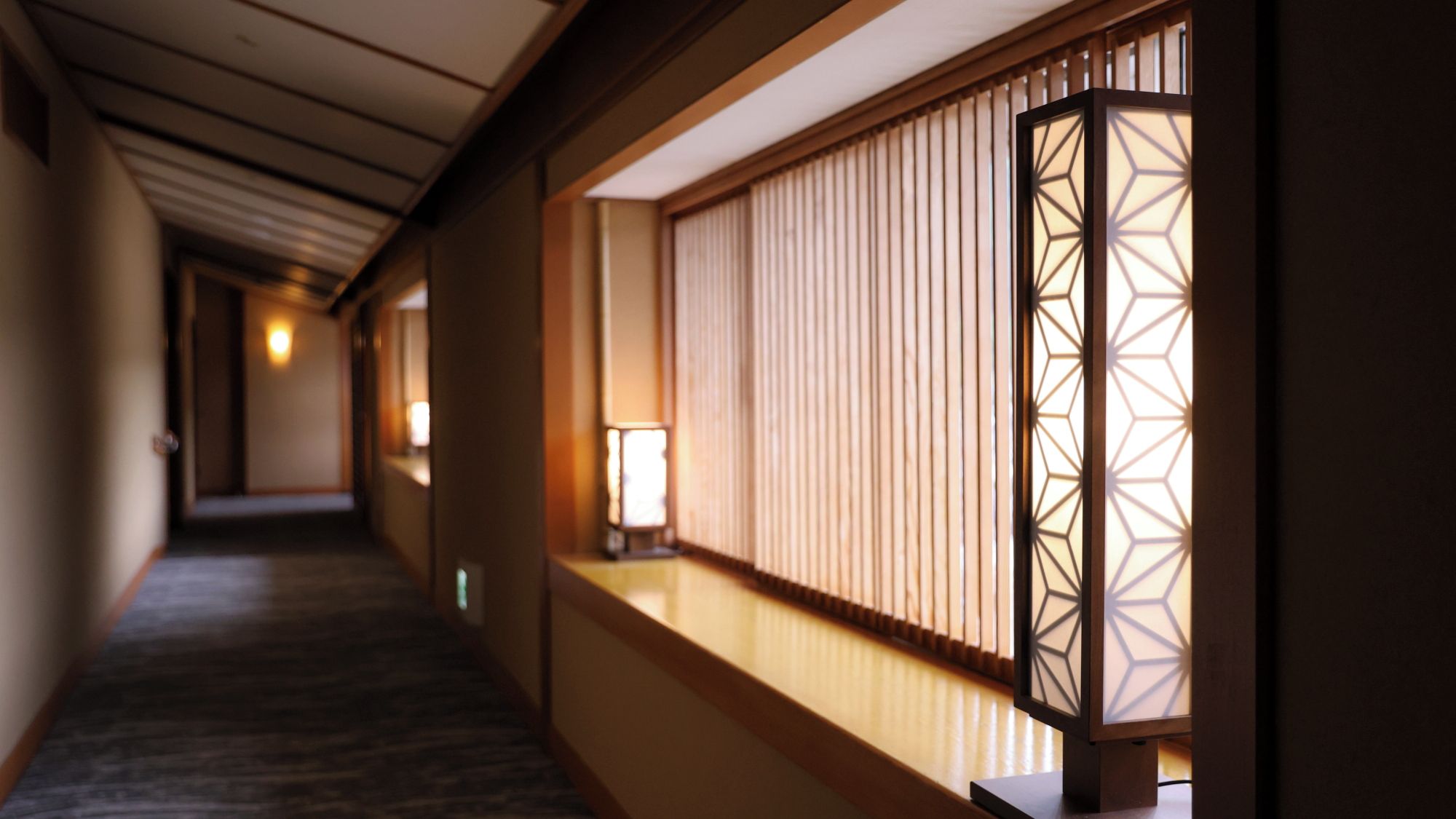 A corridor with a wooden floor, a wall with a window, and a traditional Japanese lantern.